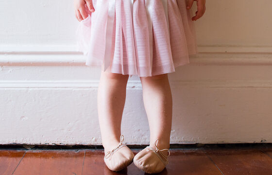 Toddler in pink tutu and ballet shoes standing in vintage hallway (cropped)